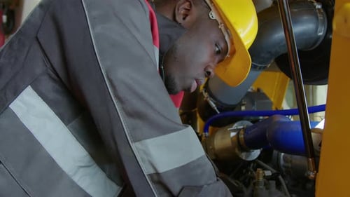 Black Factory Worker Bolting up Inside Engine Block of Tractor Frame