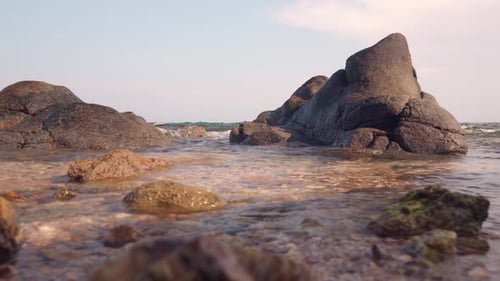Sanfte Wellen streicheln die felsige Küste, das Licht des Sonnenuntergangs erhellt das klare Wasser, der bewölkte Himmel spiegelt sich