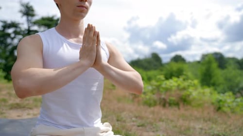 Man Meditates in Lotus Pose Folding Hands on High Grass Hill