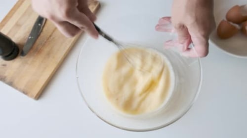 Mann verquirlt die Ei-Milch-Mischung in einer Glasschüssel in der heimischen Küche während der Zubereitung des Frühstücks