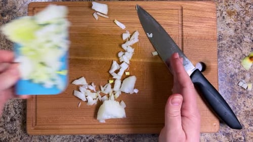 The chopped onion is removed from the wooden cutting board with a kitchen spatula
