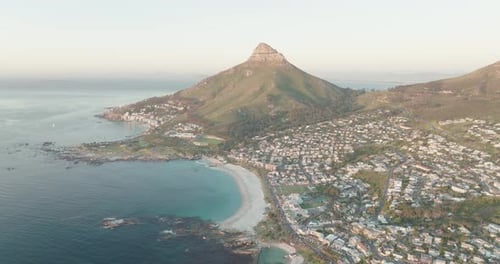 Drone flying high and sideways over the sea at Camps Bay beach in Cape Town South Africa - many hous