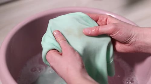 Hands Washing Stained Green Fabric in Pink Basin