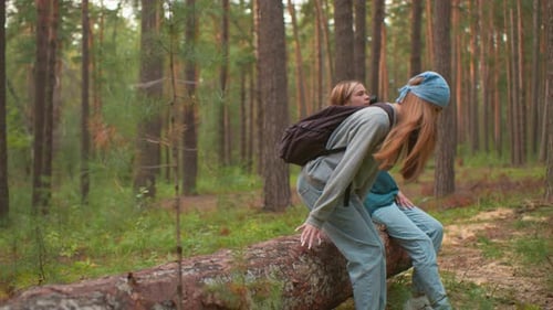 Two Tired Hikers Rest on Fallen Tree in Serene Forest