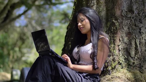 Woman Works on Laptop at Base of Tree