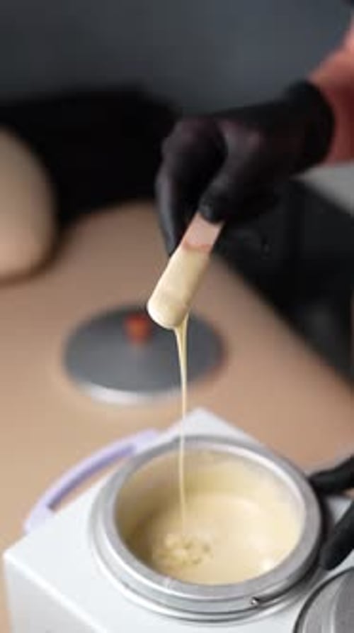 Master mixes the heating wax with a wooden spatula before the depilation procedure.