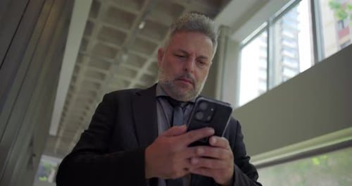 Close up of middle aged businessman in suit standing indoors using smartphone,