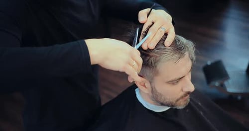 Hairdresser cuts hair to a man. Stylist making haircut with scissors. Portrait view.