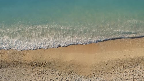 Aerial top view of footprints on golden sand with clear turquoise sea waves
