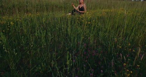 Beautiful female blonde model in black long dress sitting on a meadow