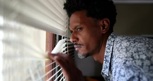 Suspicious man looking outside through window blinds