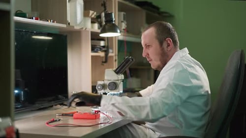 Man Analyzing Microchip Through Microscope in Office