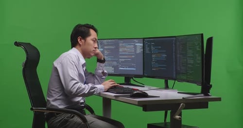 Asian Man Developer Boring While Write Code With Multiple Computer Screens In Green Screen Studio