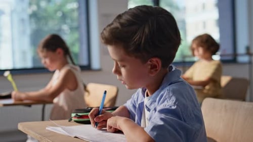 Diligent Children Writing in Classroom at Desks