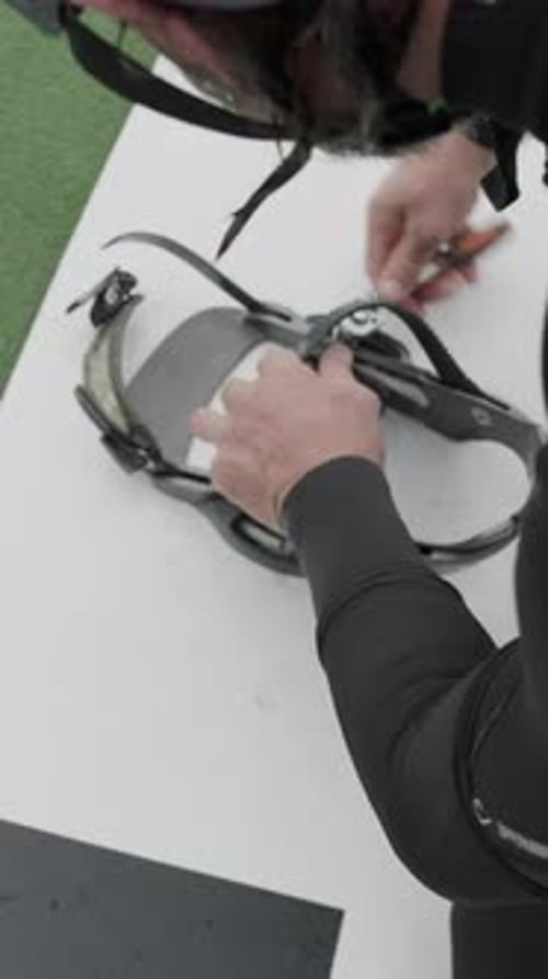 Man Tightens Wakeboard Bindings on White Surface