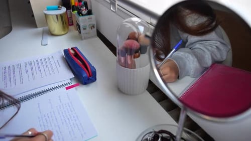 Close-up pan shot of a study desk with writing materials and makeup brushes while woman hands writes