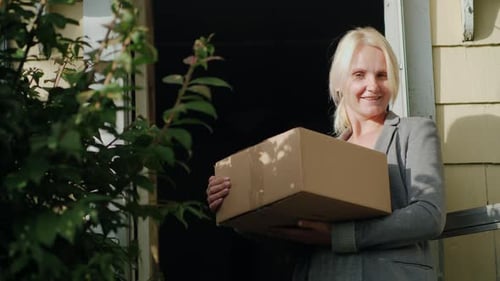 Woman Holds Box Smiling in Doorway