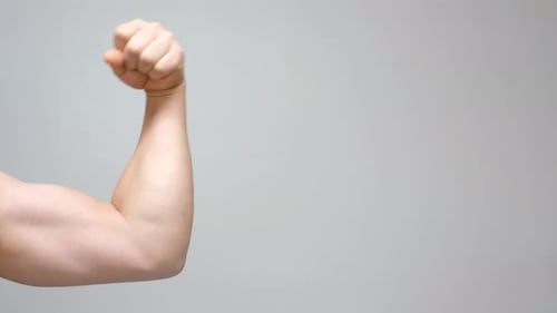 Male arm with large muscles close-up on gray background, front view.