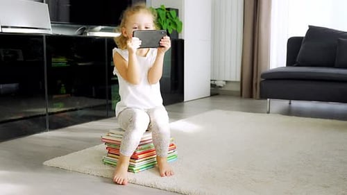 Cute Child Using Smartphone While Sitting on Books