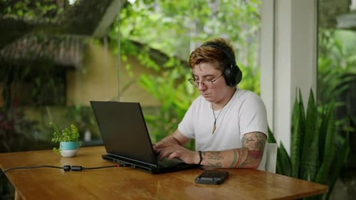 Transgender Individual Works on Laptop at Coworking Space Engrossed in Task with Headphones Green