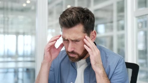 Businessman suffering from headache while sitting at workplace in business office. Upset worker hold