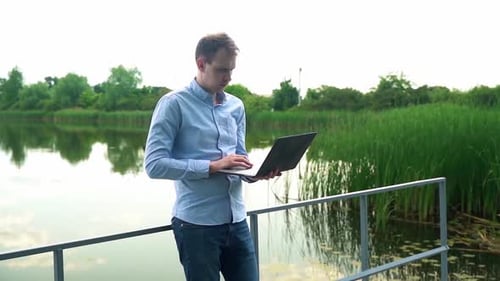 A man works with a laptop near the river