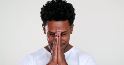 Man Puts Hands Together in Indoor Setting and Smiles