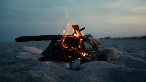 Offener blauer Himmel über einem Lagerfeuer, das im Sand brennt