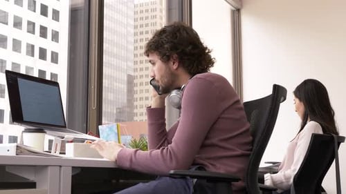 Young businessman talks on smart phone at desk in highrise office