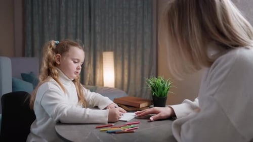 Focused Girl Drawing with Adult at a Table