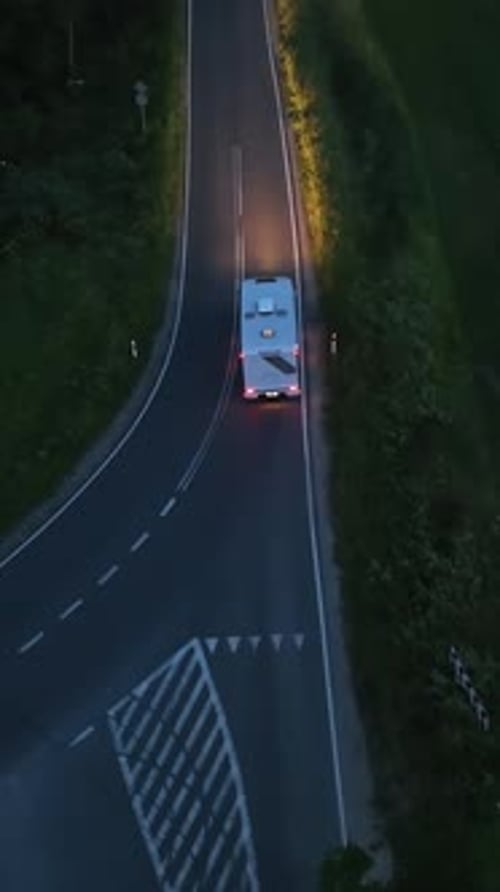 Vertical drone shot following a RV with lights on, driving on the countryside