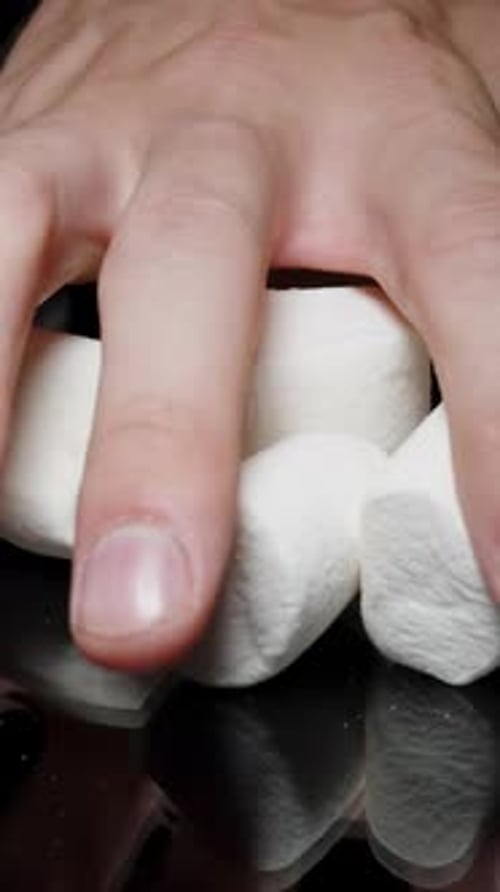 Vertical video. Close-Up of a Male Hand Taking a Pile of Marshmallows from a Black Table, Sugar