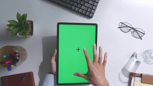 Top down view of man's hands using a mock up green screen tablet on white desk