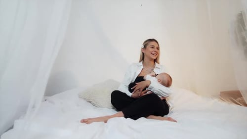 Mother Breastfeeding Baby on Bed in Home Setting