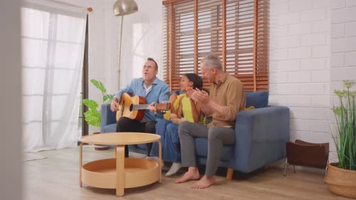 Man Plays Guitar for Child and Adult on Couch
