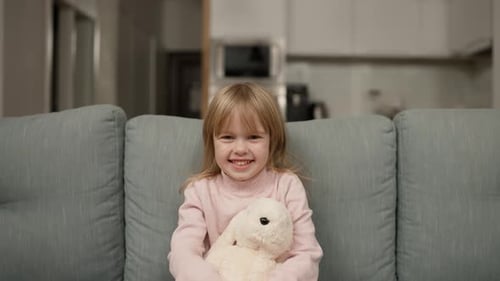 Smiling Girl with Plush Rabbit on Sofa