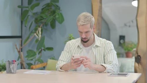 Modern Young Man Browsing Internet on Smartphone in Office