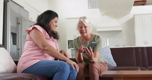 Two Women Looking at Phone on Sofa Indoors
