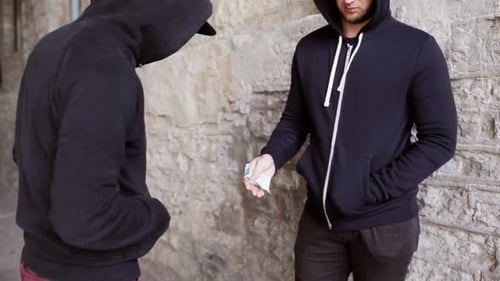 Two young men in hooded tops exchange cash