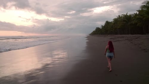 Aerial dolly in of young red hair young woman walking near the sea in Dominicalito each, overcast su