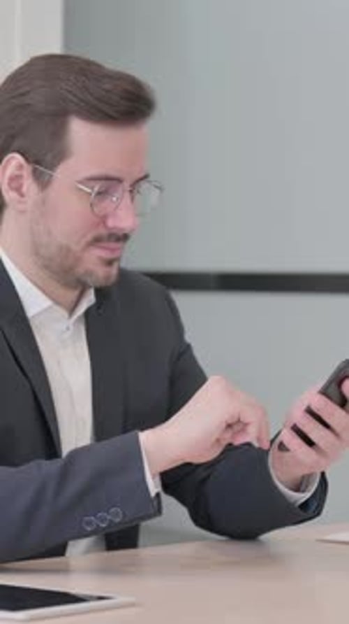 Businessman Browsing Internet on Smartphone in Office, vertical video