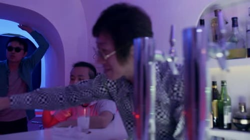 Divertido camarero japonés que sirve una bebida de una coctelera en dos vasos para dos mujeres...