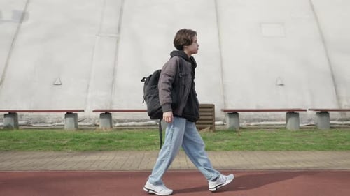 Schoolboy with a backpack walking home from school along the park path