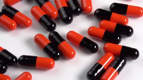 Many black and orange pills capsules or antidepressants rotating on white plate in macro top view