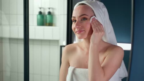 Woman Cleans Face in Bathroom with Cotton Pad
