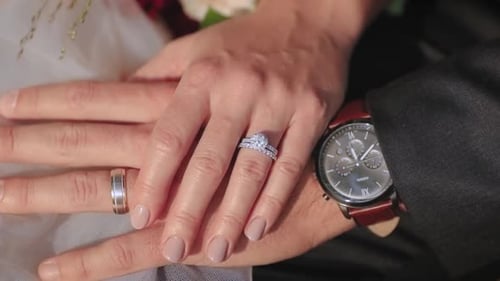 Braut und Bräutigam halten sich an ihrem Hochzeitstag an den Händen und zeigen ihre Ringe vor der Kamera.