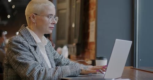 Motivated Young Businesswoman Working with Laptop Typing Indoors in Modern Cafe