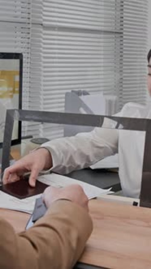 Woman Reviews Passport at Counter With Glass Barrier