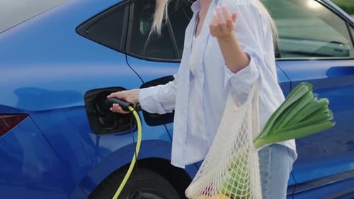 Mujer con bolsa de supermercado desconecta el cargador del coche eléctrico