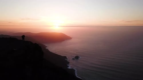 Romantic scene of couple watching sunset on edge of cliff. Aerial view